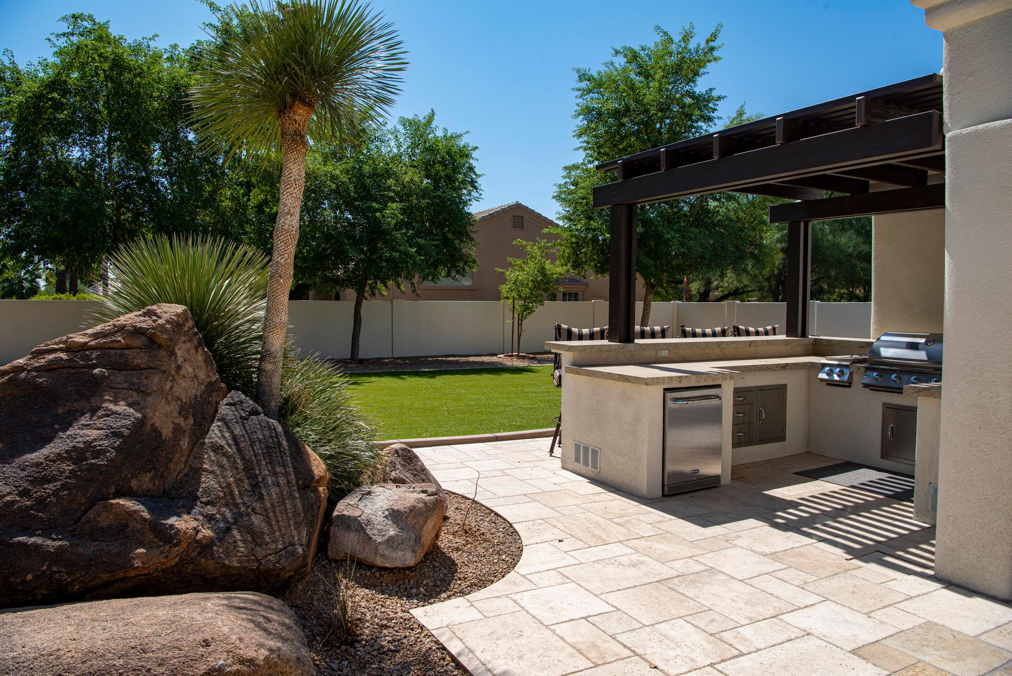 A cream travertine paver patio with an outdoor kitchen and pergola.