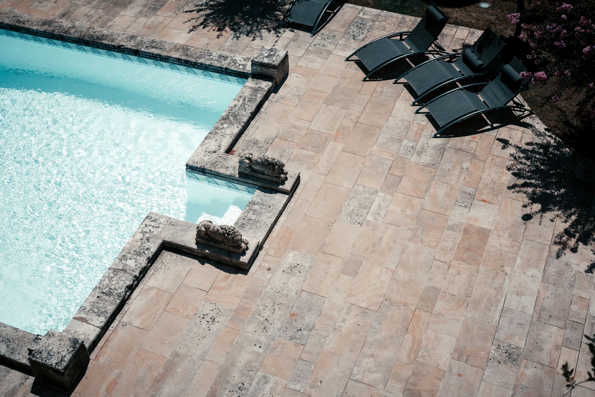 A stone-paved pool deck with loungers beside a swimming pool.