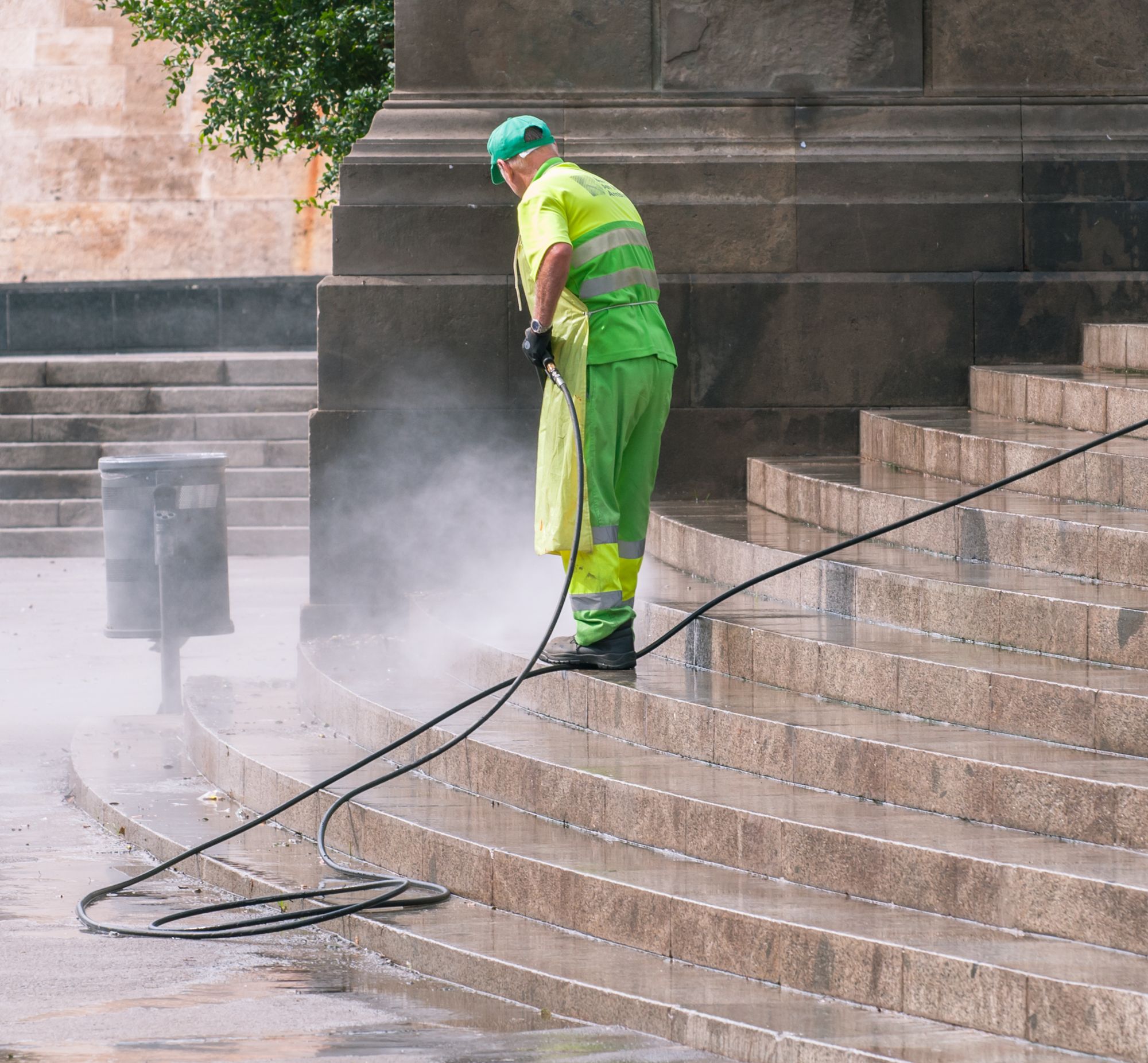 A worker pressure-washing a flight of stone steps, spray haze rising.