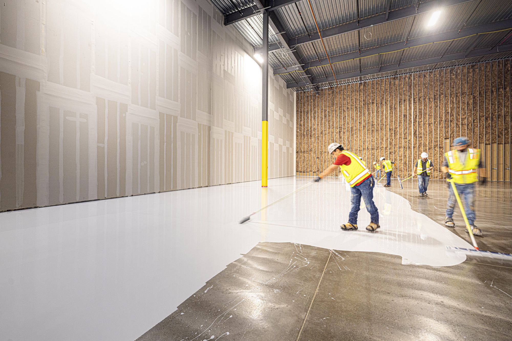 A crew spreading white epoxy across a concrete floor with squeegees.